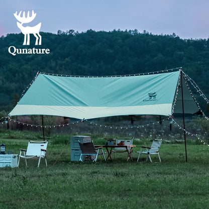 Outdoor setting with a Qunature tent, table, and chairs in a grassy field with trees in the background.